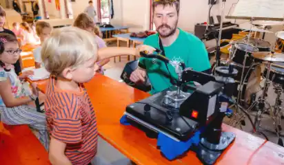 Kind probiert ein technisches Gerät unter Anleitung eines Betreuers aus.
