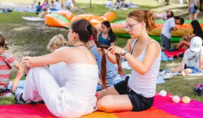 Betreuerin flechtet einem Kind die Haare auf einer Picknickdecke.