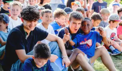 Kinder und Betreuer sitzen gemeinsam bei einer Veranstaltung im Freien.