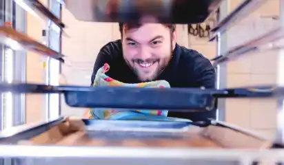 Küchenhelfer schiebt ein Tablett in einen Küchenwagen.